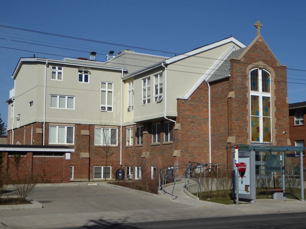 2 storeys of brick siding and two floors above that are of a ligh color. the building entrance has a ramp and a large stained glass window