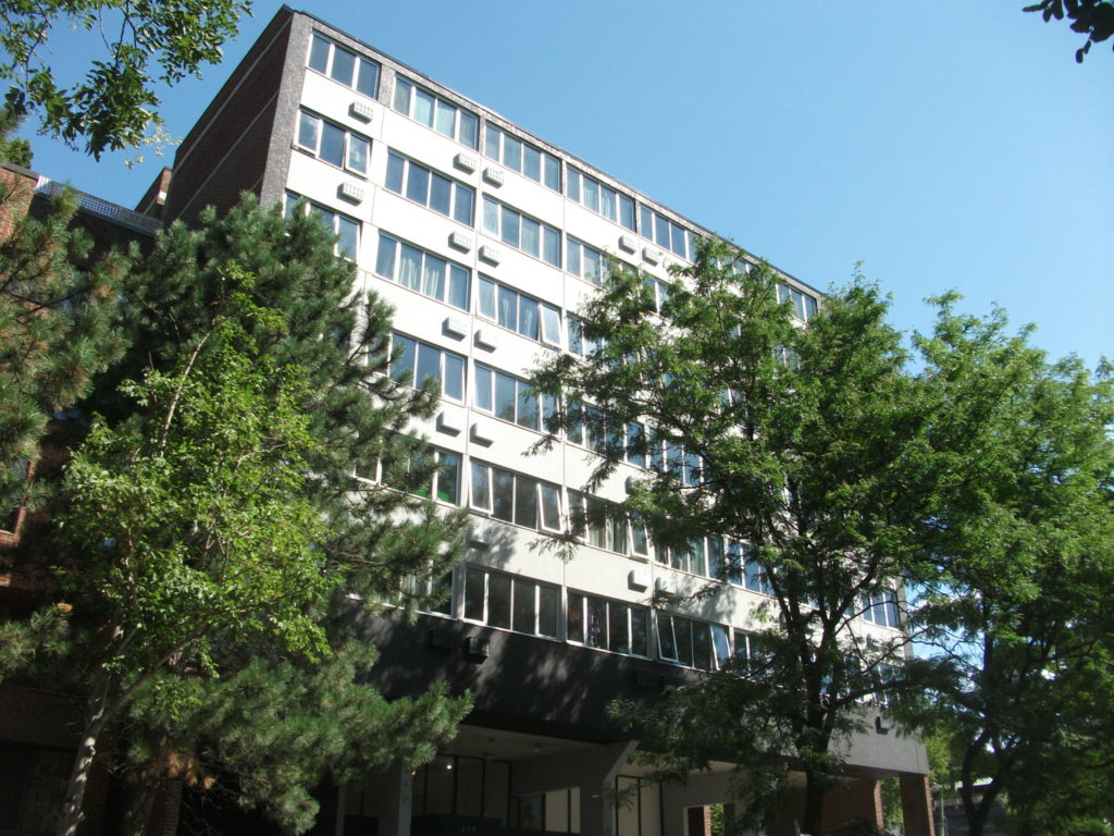 7 storey building with a brick outerface and tall green trees in the front