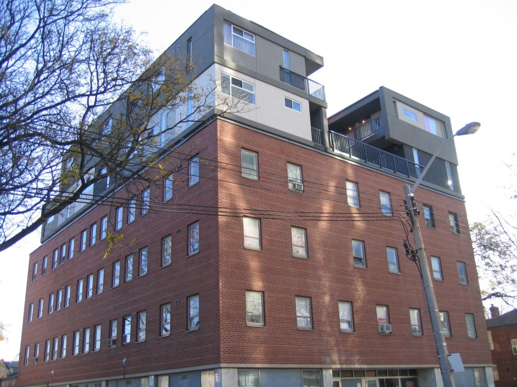 square brick building with grey top floor which has balconies